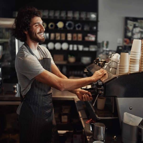 Young,Cheerful,Barista,Wearing,Black,Apron,While,Preparing,Coffee,At